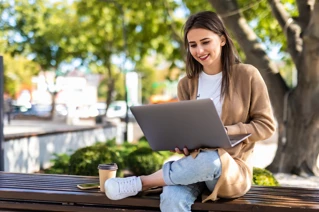 Kvinna sitter utomhus under ett träd och arbetar på en laptop