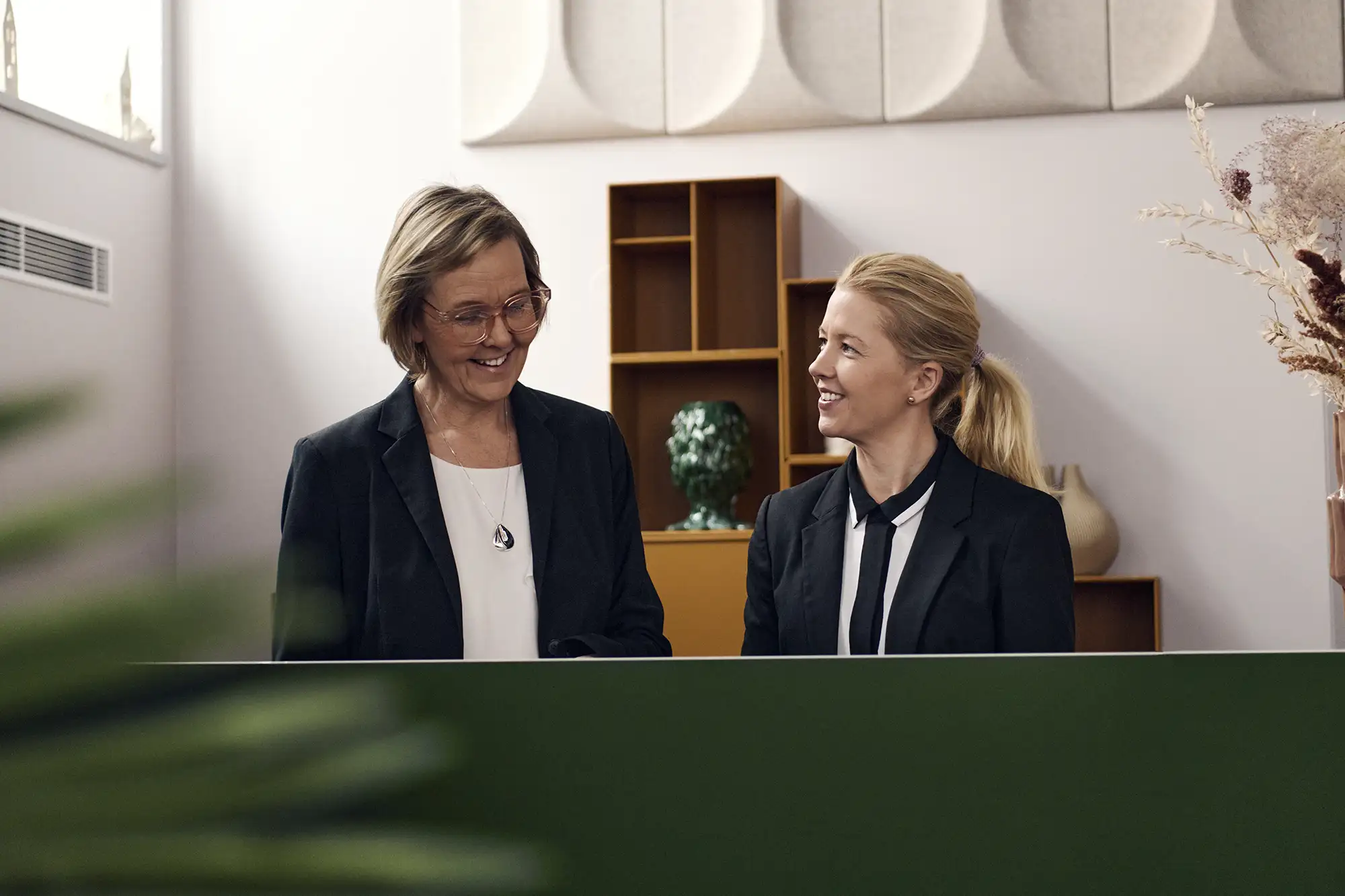 Två receptionister bakom en grön receptionsdisk