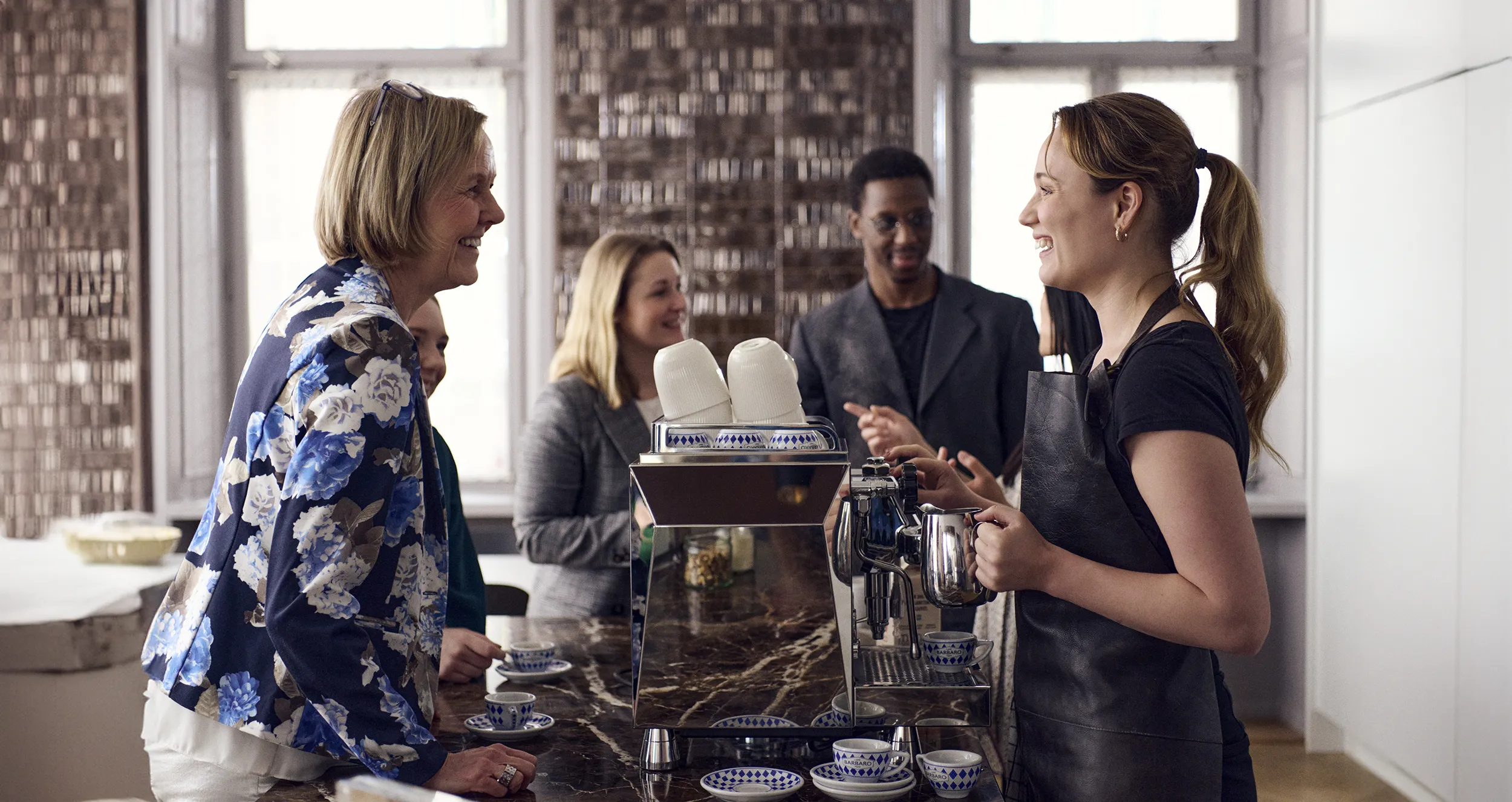 En barista serverar fyra medarbetare lyxkaffe vid en kaffedisk.